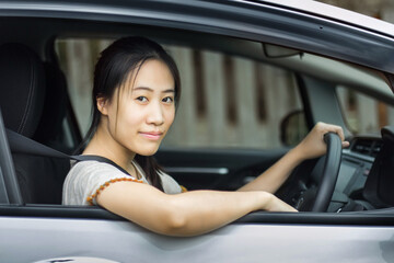 Happy Asian woman driving a car and smiling. Cute young success happy brunette woman is driving a car. Portrait of happy female driver steering car with safety belt