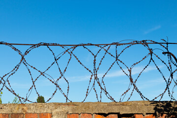 Rusty barbed wire over a brick fence against a blue sky on a sunny day