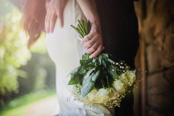 the groom hugs the waist of the bride in a white dress. hugging newlyweds close-up. bride holding white roses flowers in her hand