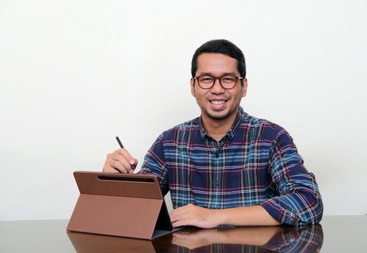 Asian man smiling to camera while working using his mobile tablet