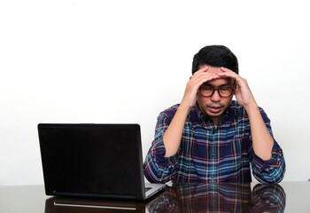 Asian man looking down languidly when sitting beside his laptop