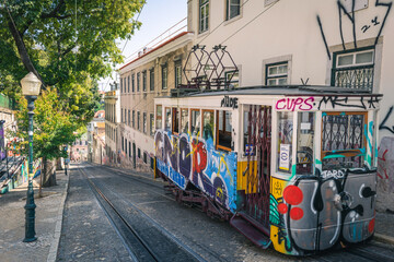 A trolley car with graffiti on it is going down the tracks in a Lisbon city street