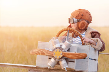 Little boy is playing plane. Happy, funy child imagines himself an aircraft pilot and plays in a aviator costume in an open-air field against a blue sky on a summer day.  Games, dreams about flying © Alexandr Vasilyev