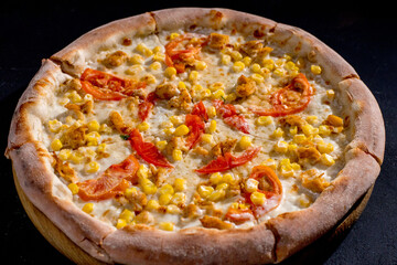 Pizza for children on a cream base with chicken fillet, tomatoes, corn and mozzarella cheese on black background