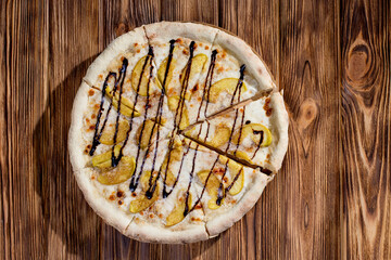 Sweet delicious pizza with apple, cinnamon, chocolate on wood background. Pizza dessert. Top view.