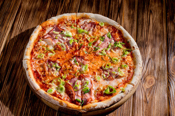 Delicious pizza with mozzarella cheese, ham, leeks on a tomato base on wood background