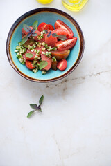 Turquoise bowl with grapefruit, tomato and cucumber salad, high angle view on a light-beige marble background, vertical shot, copyspace