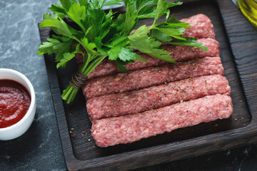 Close-up of raw serbian cevapi or cevapcici sausages with fresh parsley on a black wooden serving board, horizontal shot