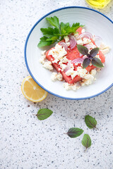 Plate with watermelon and feta cheese salad, vertical shot on a light-grey granite background, high angle view