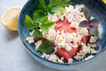 Salad with watermelon, feta cheese, red onion and fresh greens served in a blue bowl, close-up, selective focus