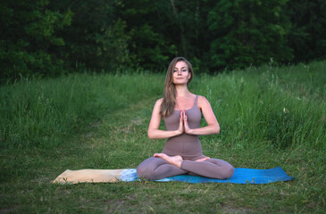 A young gymnast does yoga in nature in the park, using a combination of traditional yoga poses,...