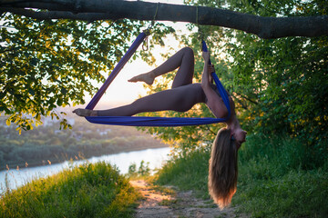 A young gymnast is engaged in aerial yoga in nature in the park, using a combination of traditional...