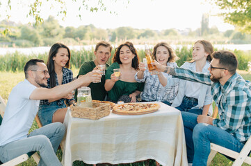 Group of friends are relaxing together outdoor. Young cheerful people clink glasses and laugh.