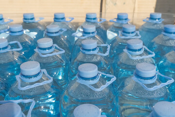 a large number of five-liter bottles of blue water with a plastic handle in the grocery store. Close-up of large bottles of mineral water.