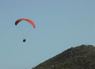 Paraglider with a red parachute flying above hills