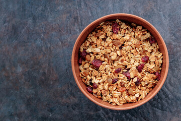 Granola with nuts and dried fruit on a dark background. Homemade granola in a clay bowl. Top view. Copy space