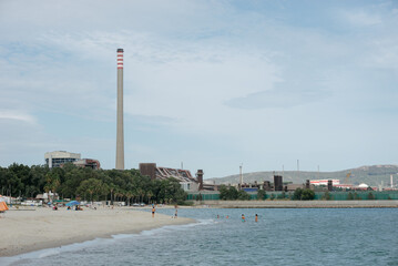 Fototapeta premium People bathing in a beach located next to a polluting industrial refinery.