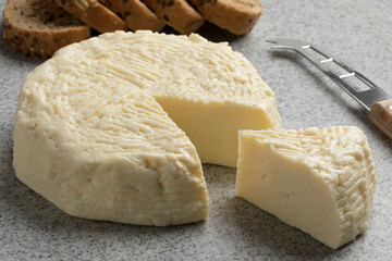 Piece of traditional Croatian homemade white cheese of cooked milk, Kuhani sirevi, on a cutting board close up 