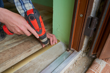 drill a hole for the dowel,a man drills a hole in the threshold of the door with a drill