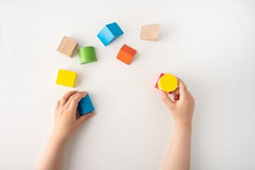 High angle shot of a child playing with colourful educational toy blocks on the table at preschool or kindergarten. Kid having fun while engaged in creative learning and development
