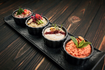 A variety of vegetable appetizers, on black plates on a wooden background