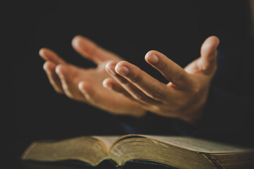 Hand folded in prayer to god on Holy Bible book in church concept for faith, spirituality and...