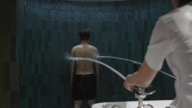 In modern clinic shot back man enjoys anti-cellulite treatment experiencing Charcot douche in spa salon. Water around. Slow motion
