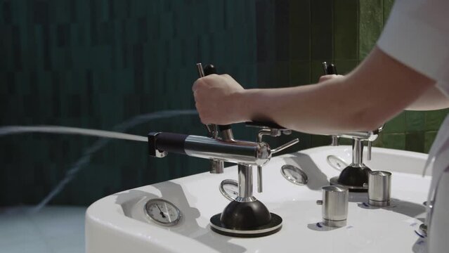 Close up hands of nurse regulate Charcot douche equipment at spa center. Pressurized water jets for water massage. Slow motion