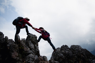 Person hike friends helping each other up a mountain. Man and woman giving a helping hand and...