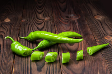 Green hot chili peppers with slices on wooden background