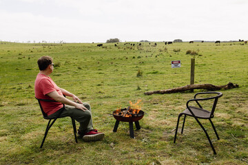 A man sitting by a lit fire next to a paddock in Australia