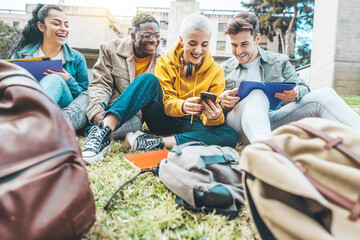 Group of multiracial students having fun sitting in college campus together - Happy teenagers using...