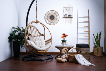 Unique living room interior with stylish hanging rattan chair, design furniture, plants, wooden floor, decoration and elegant personal accessories.