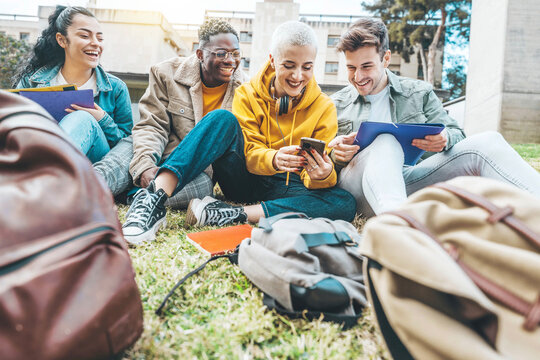 Group of multiracial students having fun sitting in college campus together - Happy teenagers using smart mobile phone outside - Millenial people laughing oudoors - Scholarship concept