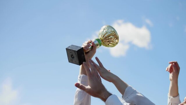 Single hand with a white sleeve holds golden cup trophy high in the air, other hands try and fail to grab it. The best, business competition winner, unreachable industry leader, concept.