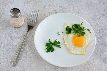 fried egg with yellow yolk on white plate with chopped parsley, close-up