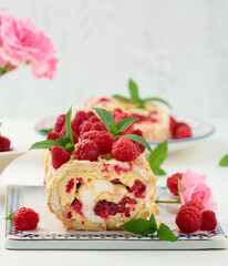 Baked meringue roll with cream and fresh red raspberry on a black wooden board