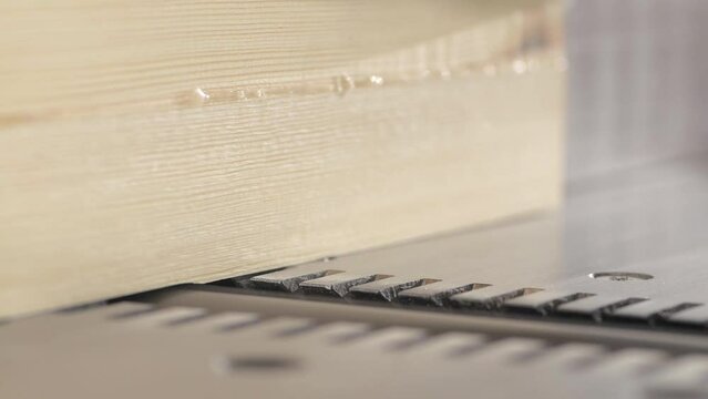 Slow motion shot of a carpenter trimming a board using a thickness planer, wooden shavings and dust flying out during the wood processing. Carpenter planing of board. Close up.
