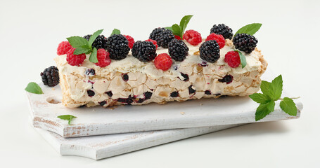 Baked meringue roll with cream and fresh fruits on a white wooden board, delicious dessert