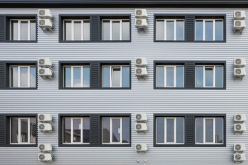 Many air conditioners hang on facade of new modern building.