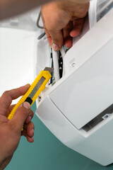 Male electrician with stationery knife cuts and strips wires while installing air conditioner.