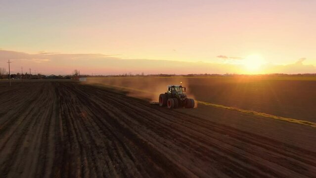 tractor working plowing the field at sunset dusk aerial view drone,summer sunny day
