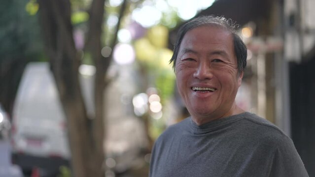 Portrait of a happy senior Asian man smiling at camera standing in city street. Closeup older joyful person face