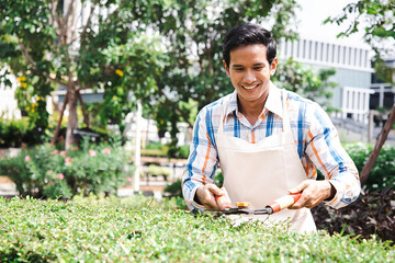 Young handsome man gardener smiling happy caring plants using pruning shears in terrace at garden