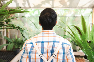 Fototapeta premium Back view, Portrait of confident male gardener standing with arms crossed at greenhouse, working with garden tools on his farm near countryside house.