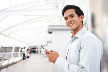 Young Asian business man smile holding smart phone at middle of cityscape area,man smart business concept.