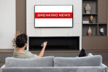 Back view on excited man sitting on the couch and watching breaking news on tv at home