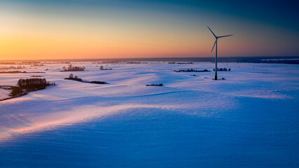 Wonderful snowy field and wind turbine at sunrise in winter