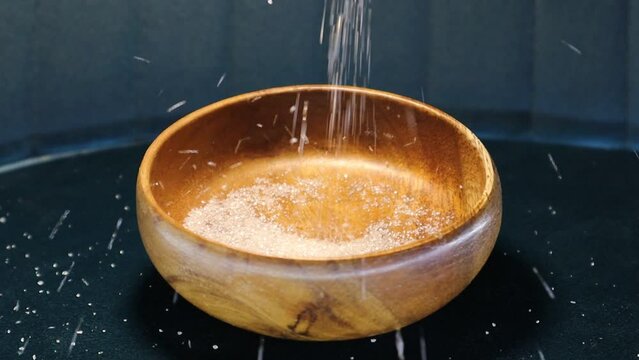 Sugar particles pour from above into a wooden plate and bounce off it, falling nearby. the video concept is also suitable for products such as citric acid, oxalic acid, magnesium sulfate, epsom salt