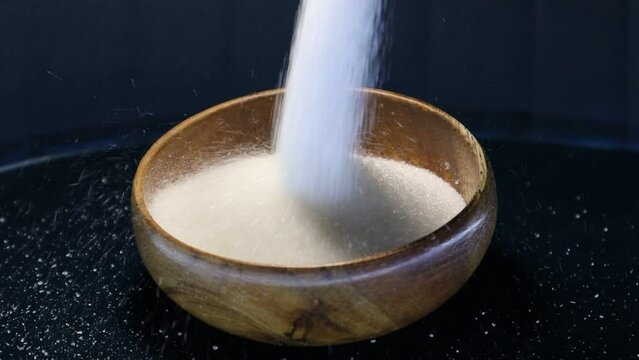 White sugar crystals pour from above in a thick stream into a wooden plate and form a slide. the video concept is also suitable for products such as citric acid, oxalic acid, magnesium sulfate, epsom 